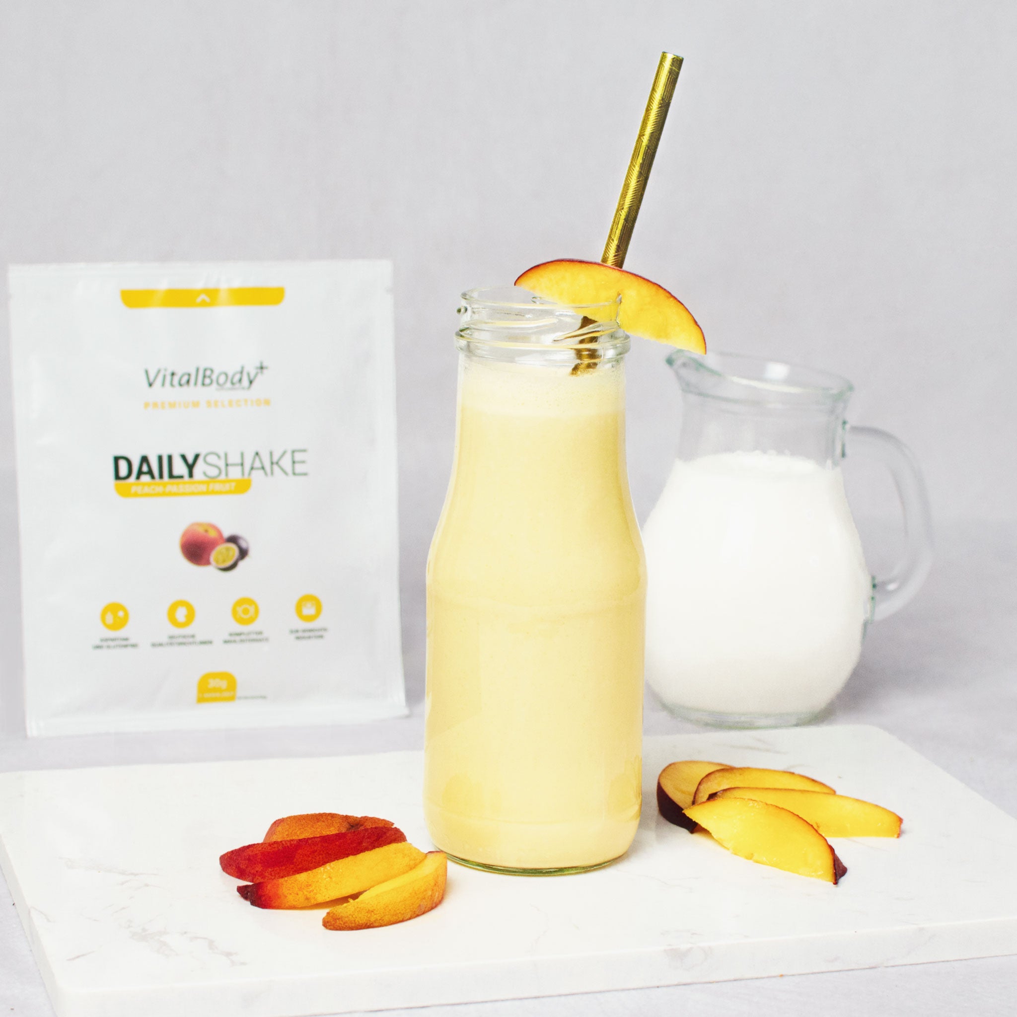Glasflasche mit Shakeinhalt Peach-Passion Fruit mit Pfirsichscheiben auf einer Marmorplatte im Hintergrund ein DailyShake To Go Pack Peach-Passion Fruit und einer Karaffe mit Hafermilch