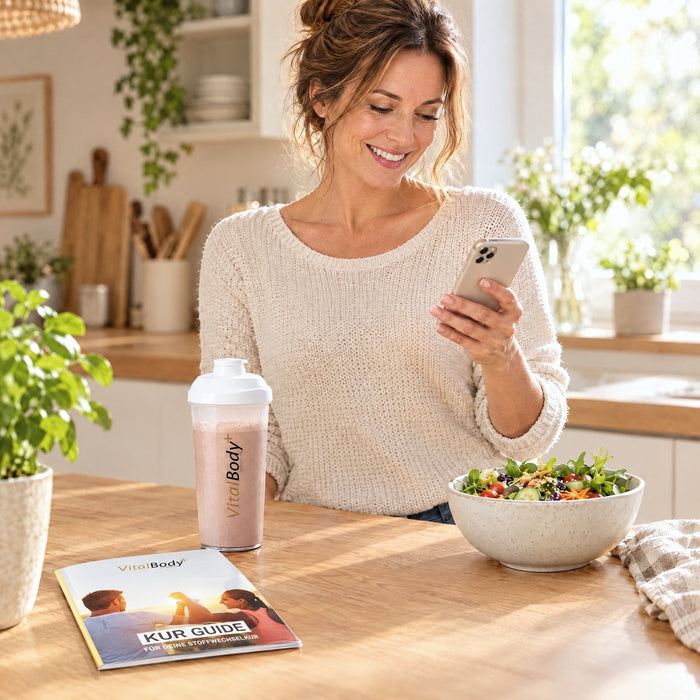 Frau in der Küche mit Kur Guide, Shaker und Salat liest eine Nachricht auf dem Handy
